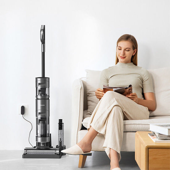 Black cordless vacuum cleaner, Dreame H11 Max, next to woman on couch.