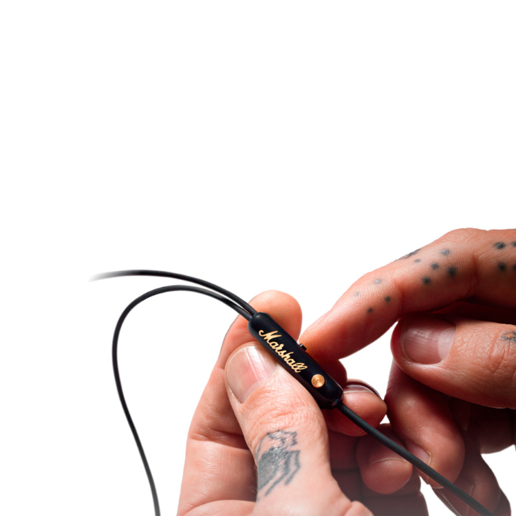 Auriculares Marshall Mode EQ preto com fios sendo segurados por mãos com tatuagens.