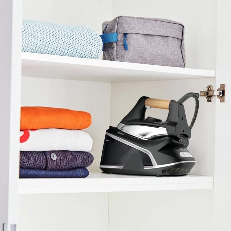 Black Rowenta iron with wooden handle on shelf next to folded clothes.