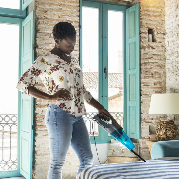 Woman using Cecotec Conga Popstar 1000 Duostick handheld vacuum on bed.