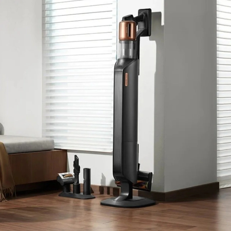 Black cordless vacuum cleaner, Dreame Z20, with copper accents, standing on wooden floor next to charging dock.