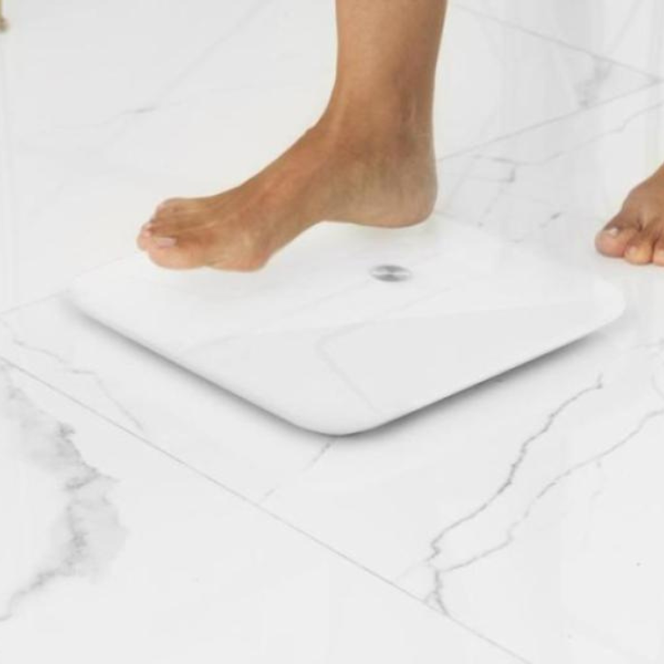 White Cecotec smart scale on marble floor, person stepping on.
