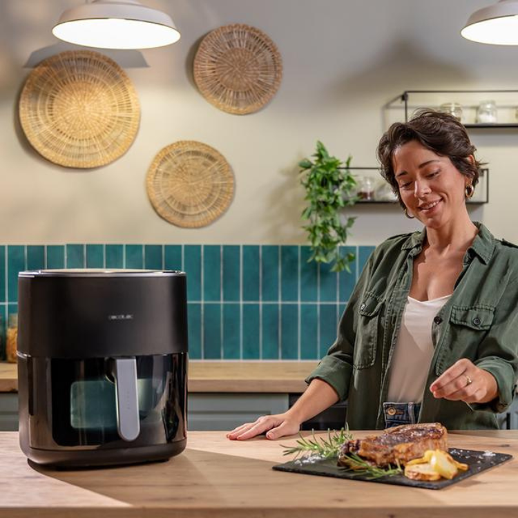 Black Cecotec air fryer on kitchen counter with woman preparing food.