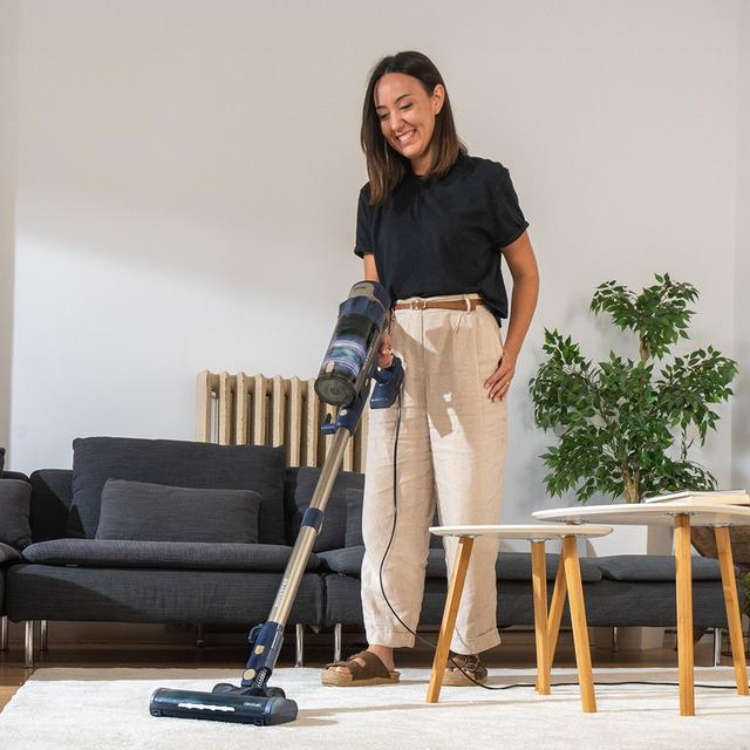 Cecotec Conga Rockstar 800 vacuum cleaner, black and blue, being used by a woman on a white rug.