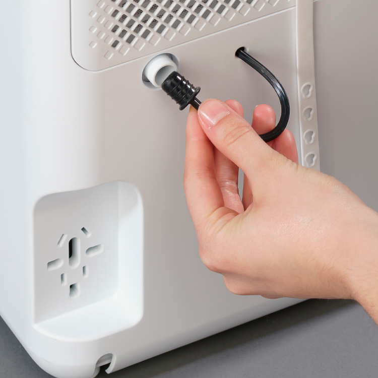 White Jocel dehumidifier with hand plugging in drain hose.