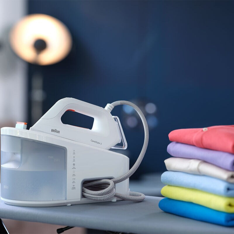 White Braun Carestyle 3 ironing machine with boiler, 2400W, next to folded colorful clothes.