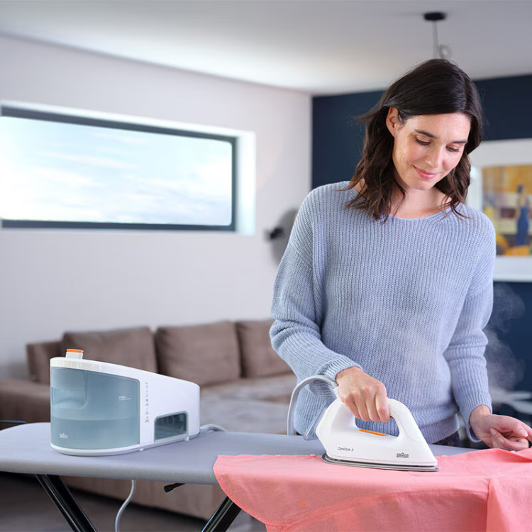 Woman ironing pink fabric with white Braun Carestyle 3 iron and boiler.