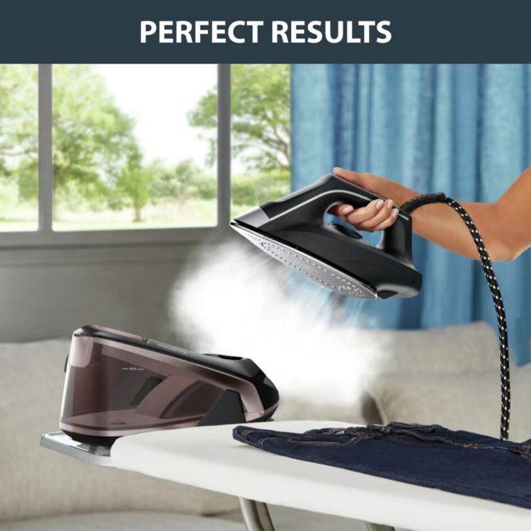 Black Rowenta steam iron on ironing board with steam.