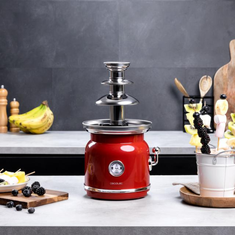 Red Cecotec Fun Chocolicious 90W chocolate fountain with silver accents on kitchen counter.