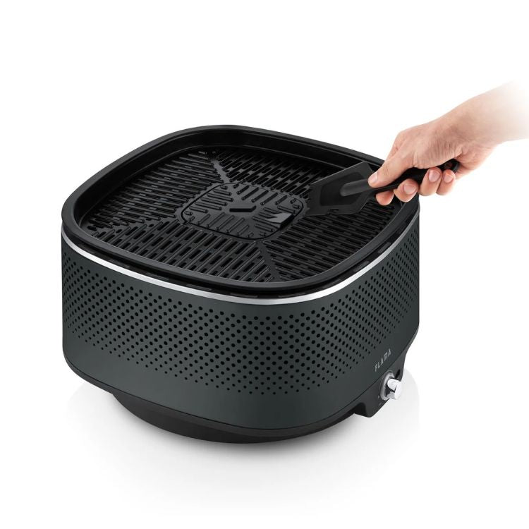 Grelhador a carvão Flama Mastergrill EVO 4011FL preto com uma mão a segurar uma pá.