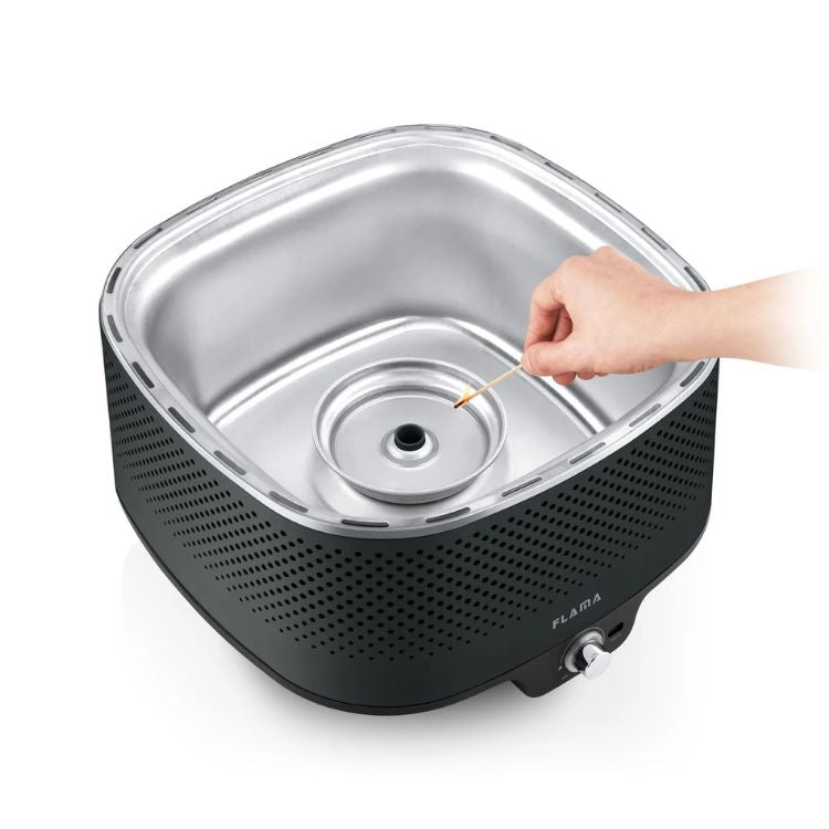 Grelhador a carvão Flama Mastergrill EVO 4011FL preto com uma mão a acender o carvão.