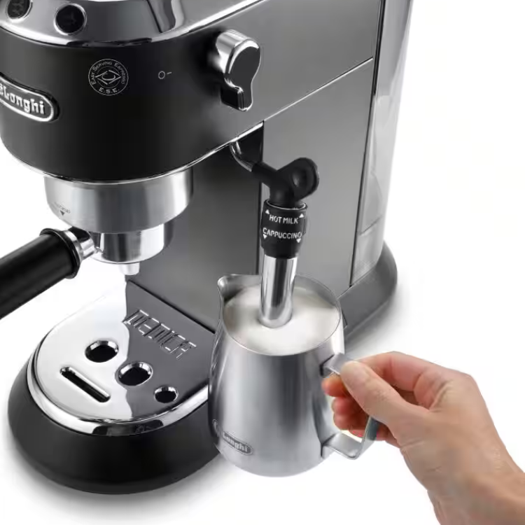 De'Longhi Dedica espresso machine with black and stainless steel body, hand holding steaming pitcher.
