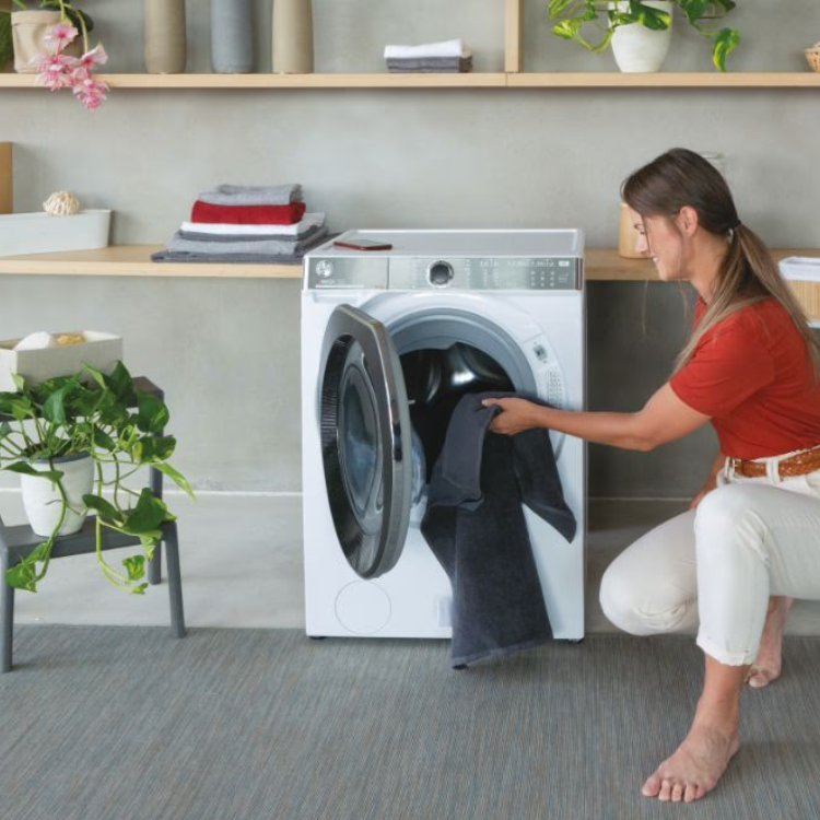 Woman loading dark clothes into white Hoover front-loading washing machine.