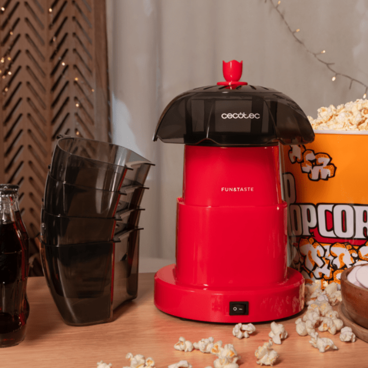 Red Cecotec Fun&Taste P'Corn Lotus popcorn maker with black top, on wooden table with popcorn and snacks.