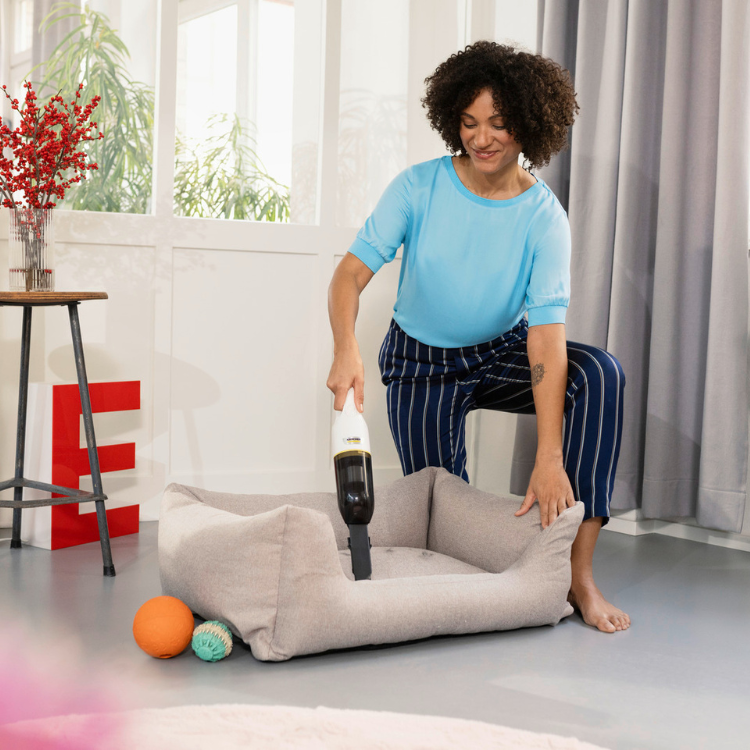 Aspirador de mão sem fios Karcher CVH 2, mulher a limpar cama de cão com ele.