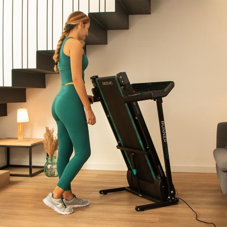 Woman in green workout gear on Cecotec DrumFit WayHome 1000 Runner Sprint black treadmill.