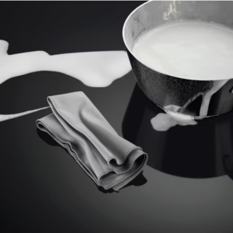 AEG induction cooktop with 3 zones, 60cm, black, with a pot of milk and cloth.