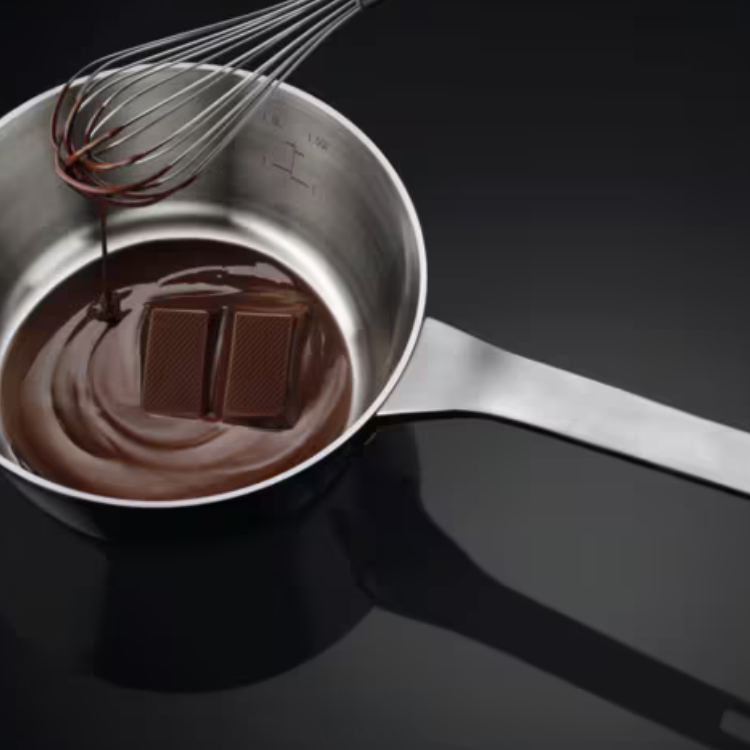Stainless steel saucepan with melted chocolate and two chocolate bars, whisk pouring chocolate.