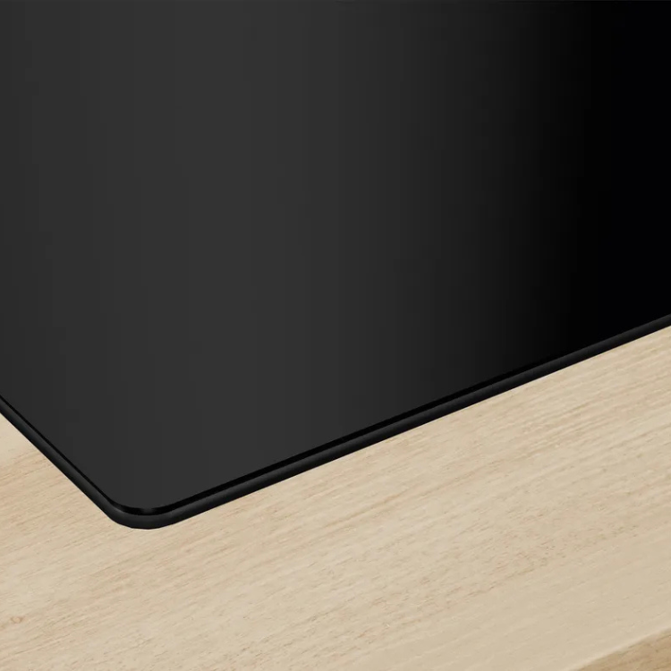 Black induction cooktop corner on light wood surface, Bosch Serie 4.