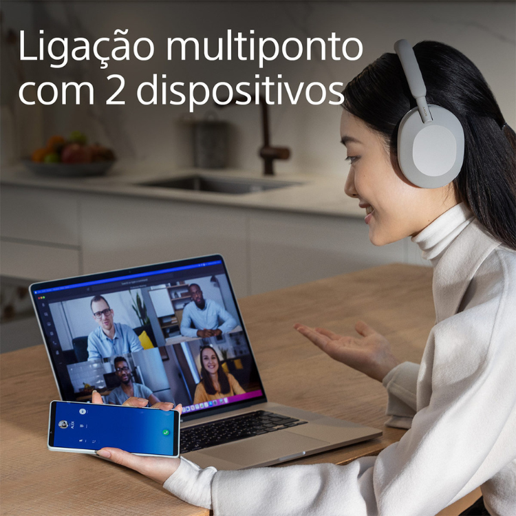 Woman wearing white Sony over-ear headphones, on video call with laptop and phone.