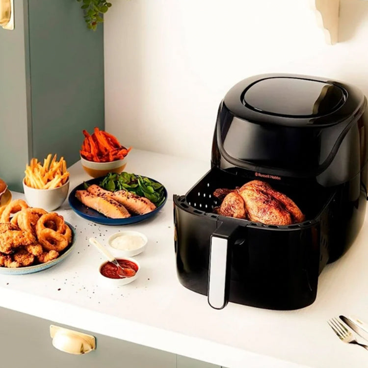 Black Russell Hobbs air fryer with cooked chicken inside, on white countertop with various fried foods.