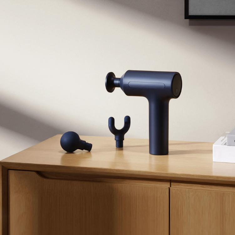 Xiaomi Massage Gun 2, dark blue massage gun with two attachments on a wooden cabinet.